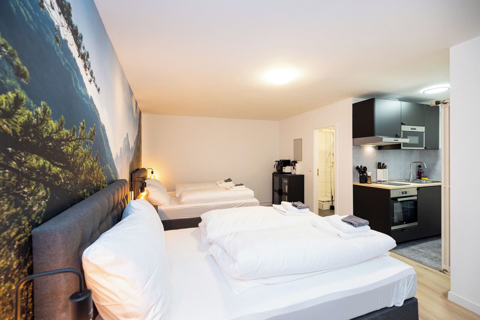 A hotel room with two beds, a kitchenette, and a bathroom.