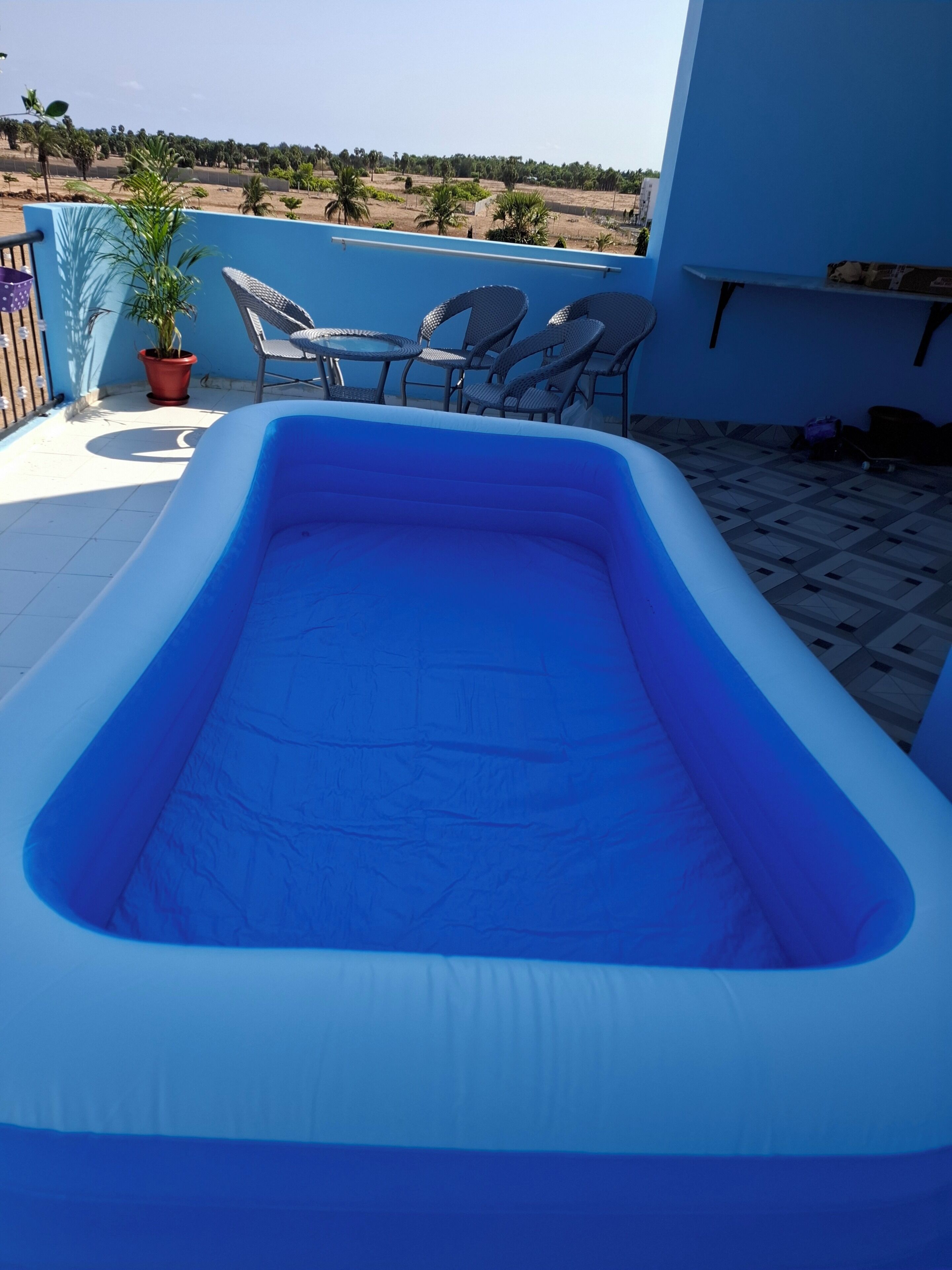 Uma piscina inflável com interior azul, cercada por uma parede azul e um vaso de planta.