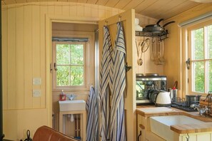 Une cuisine avec des meubles en bois, un four à micro-ondes, une bouilloire et une fenêtre donnant sur un paysage verdoyant.