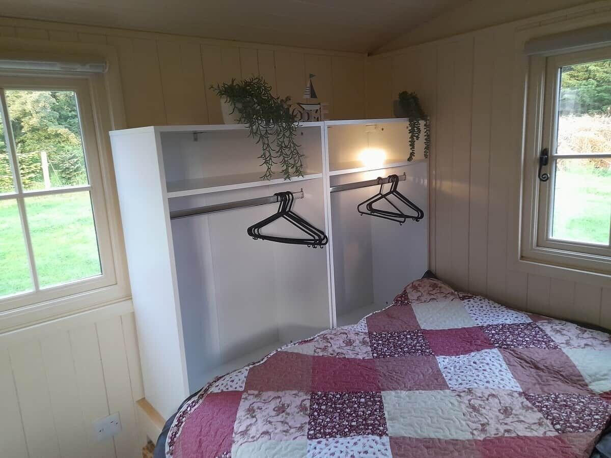 Ein Schlafzimmer mit einem Bett, einem Kleiderschrank und einem Fenster mit Blick auf Grünflächen.