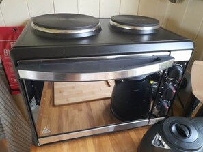 Une cuisine compacte équipée d’un four encastré, d’une machine à café et d’une planche à découper en bois.