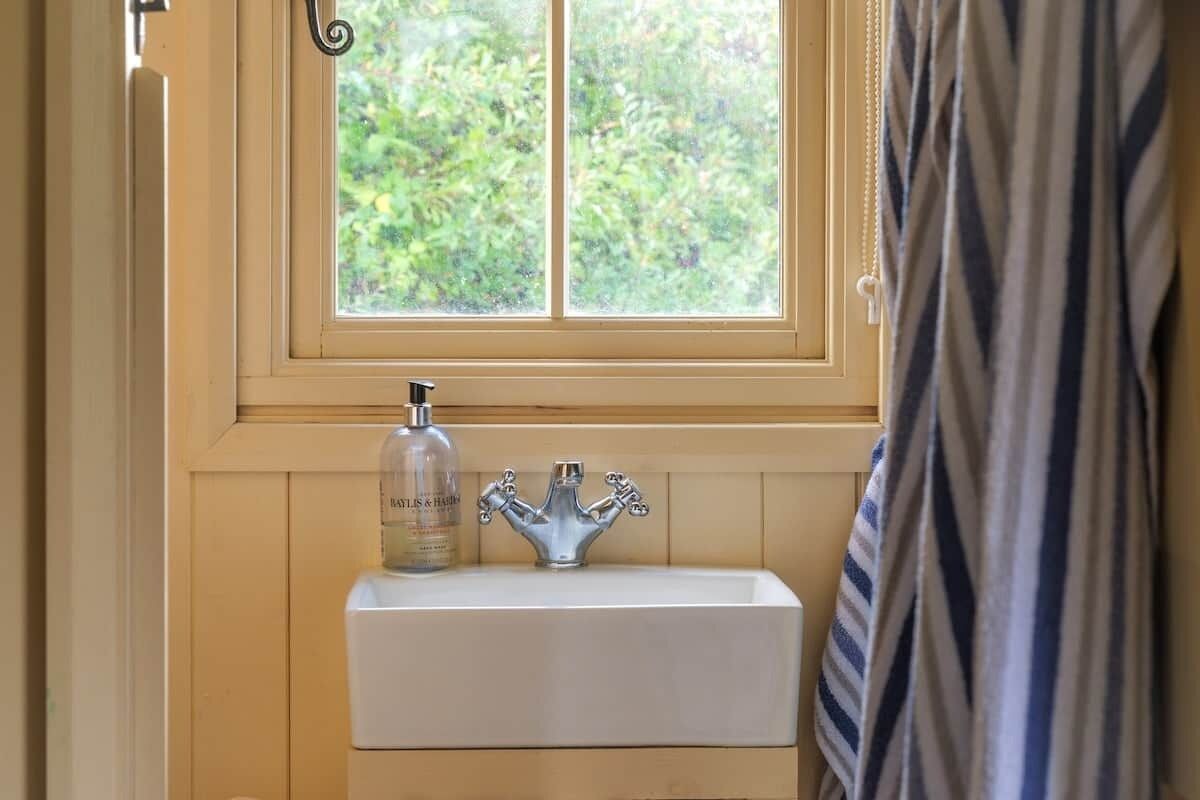 Une salle de bain avec une fenêtre, un lavabo et un flacon de savon pour les mains.