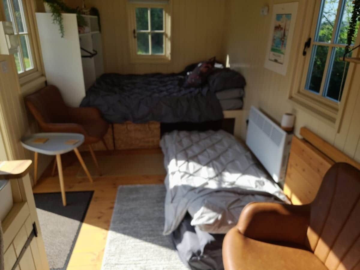 A compact room with a bed, a small table, a chair, and a radiator.