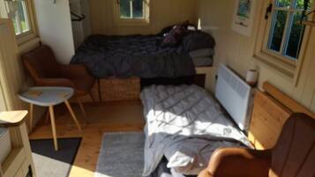 A compact room with a bed, a small table, a chair, and a radiator.