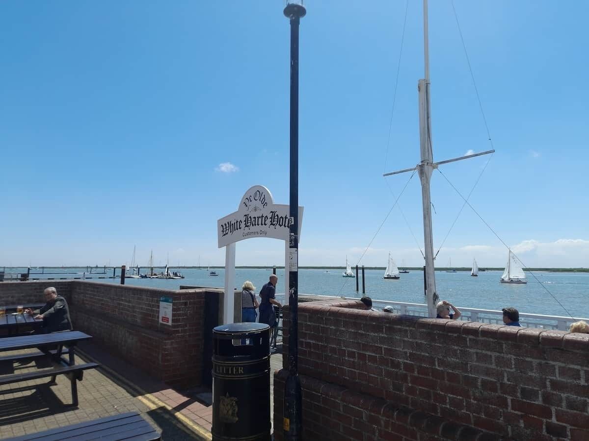 A waterfront restaurant with a sign for 'White Hart Hotel' and a view of sailboats on the water.