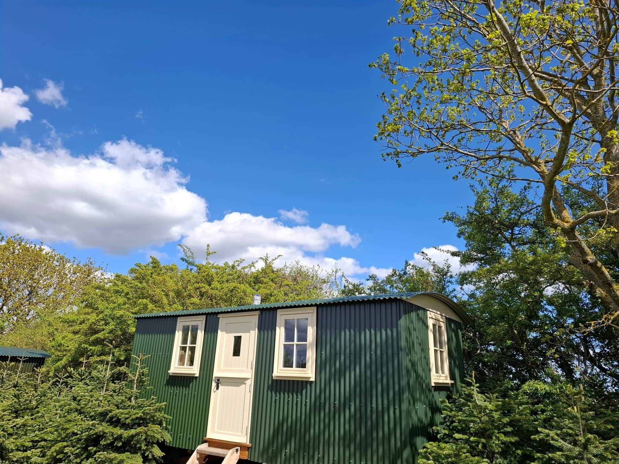 A small, single-story building with a green exterior and white trim, surrounded by lush greenery and trees.