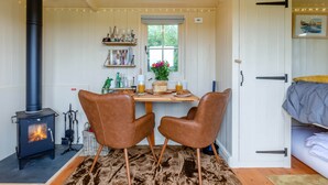 Een knus vertrek met een houtkachel, twee leren fauteuils, een eettafel met ontbijtspullen en een bed met dekbed.