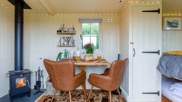 A cozy room with a wood-burning stove, two leather chairs, a dining table with breakfast items, and a bed with a blanket.