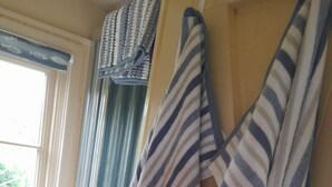 Een kamer met gestreepte handdoeken aan een rek, een raam met gordijnen, en een witte stoel.