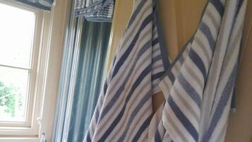 A room with striped towels hanging on a rack, a window with curtains, and a white chair.