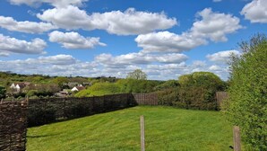 Een landelijk landschap met een stenen muur, een begraasd veld en verspreide bomen onder een lichtbewolkte lucht.