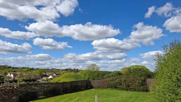 A rural landscape with a stone wall, grassy field, and scattered trees under a partly cloudy sky.