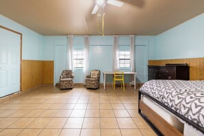 Ein Schlafzimmer mit einem Bett, zwei Stühlen, einem Tisch und einem Deckenventilator.
