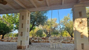 An outdoor covered area with a swing chair, stone wall, and trees. - A cozy villa with all the amenities and an outdoor gazebo. (Puglia)