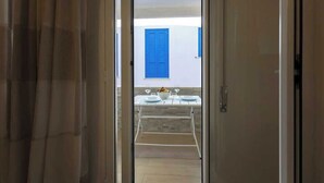 An open door leading to a balcony with a table set for two, a blue shuttered window, and a white wall. - A cozy home in a quiet part of town, 200 meters from the sea as the crow flies (Marettimo)