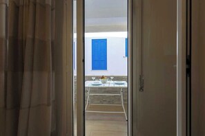 An open door leading to a balcony with a table set for two, a blue shuttered window, and a white wall. - A cozy home in a quiet part of town, 200 meters from the sea as the crow flies (Marettimo)