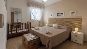 A bedroom with a wooden crib, a bed with a headboard, a nightstand, a bedside table, and a ceiling fan. - A cozy home in a quiet part of town, 200 meters from the sea as the crow flies (Marettimo)