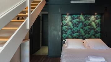 Een slaapkamer met een bed, witte kussens, een nachtkastje, een houten trap en een wand met een bladmotief.