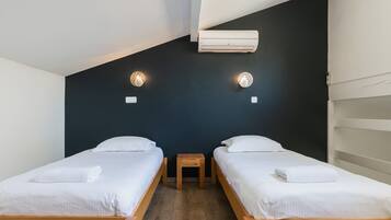 Una stanza con due letti di legno, un comodino in legno e un condizionatore d'aria fissato alla parete.