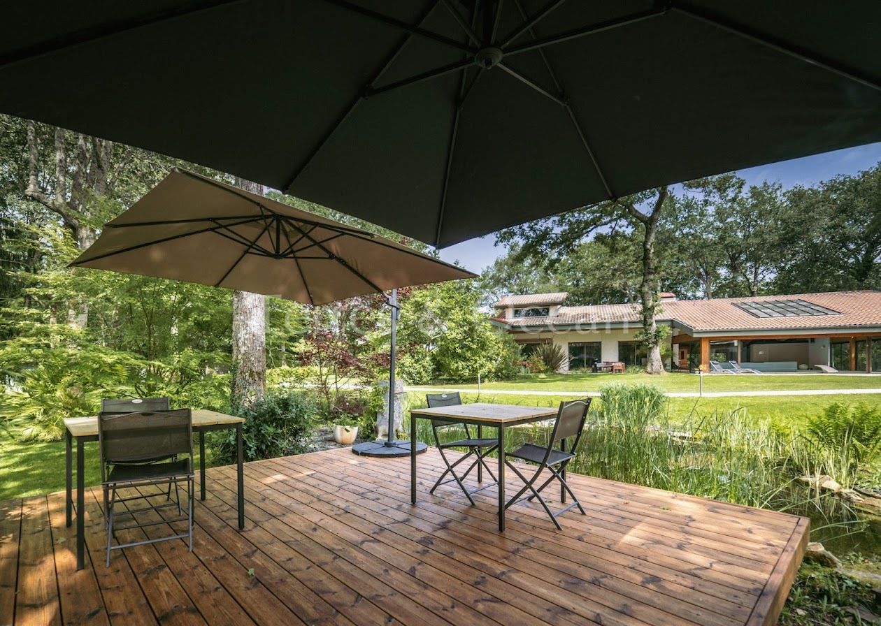 Un patio al aire libre con una mesa, sillas, un paraguas grande y una vista de una casa al fondo.