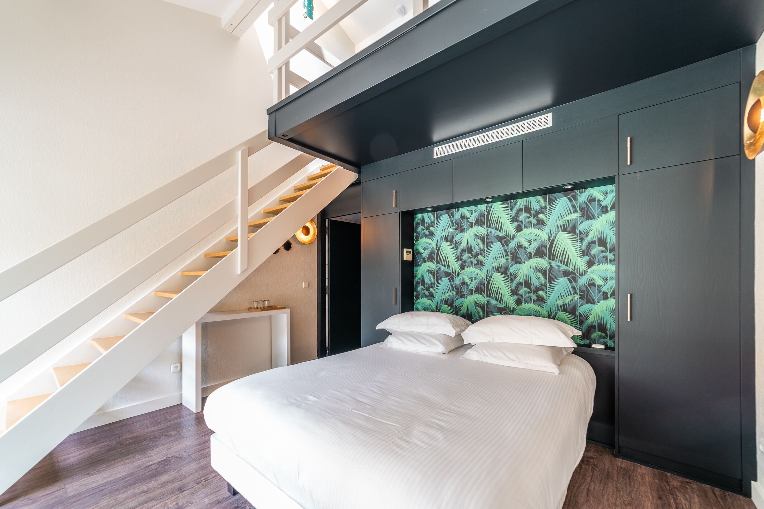 Ein Schlafzimmer mit einem Bett, einem Blattmuster-Kopfende, einer Treppe und einem Kleiderschrank.