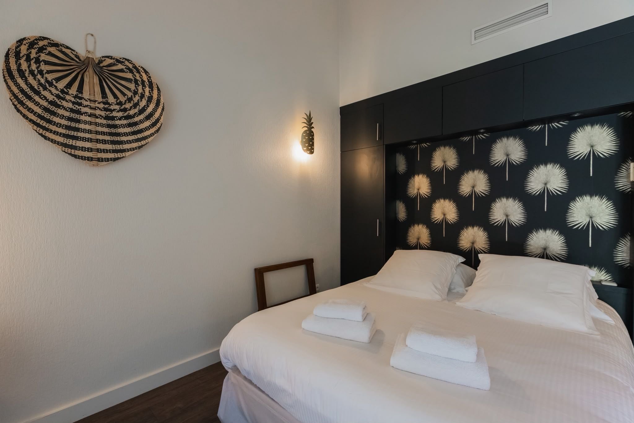 A hotel room with a bed, white linens, a heart-shaped wall hanging, and a wall with a dandelion pattern.