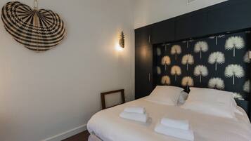A hotel room with a bed, white linens, a heart-shaped wall hanging, and a wall with a dandelion pattern.
