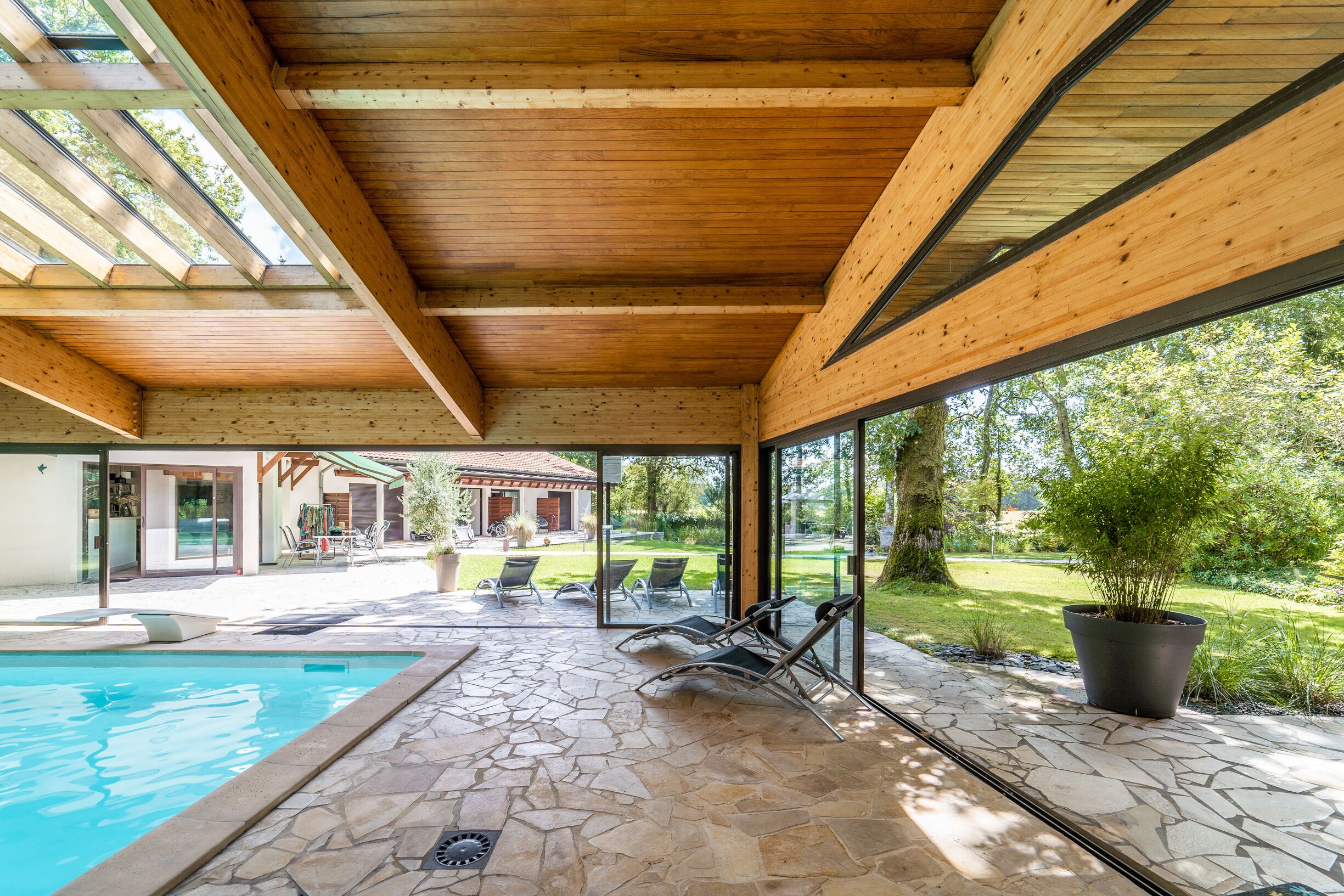 Un espace extérieur abrité comprenant une piscine, un sol en pierre et une vue sur une maison et un jardin.
