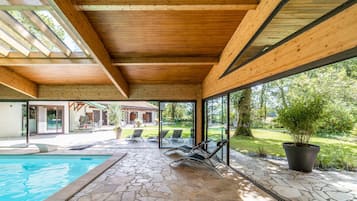 Un espacio al aire libre cubierto con piscina, suelo de piedra y vistas a una casa y jardín.
