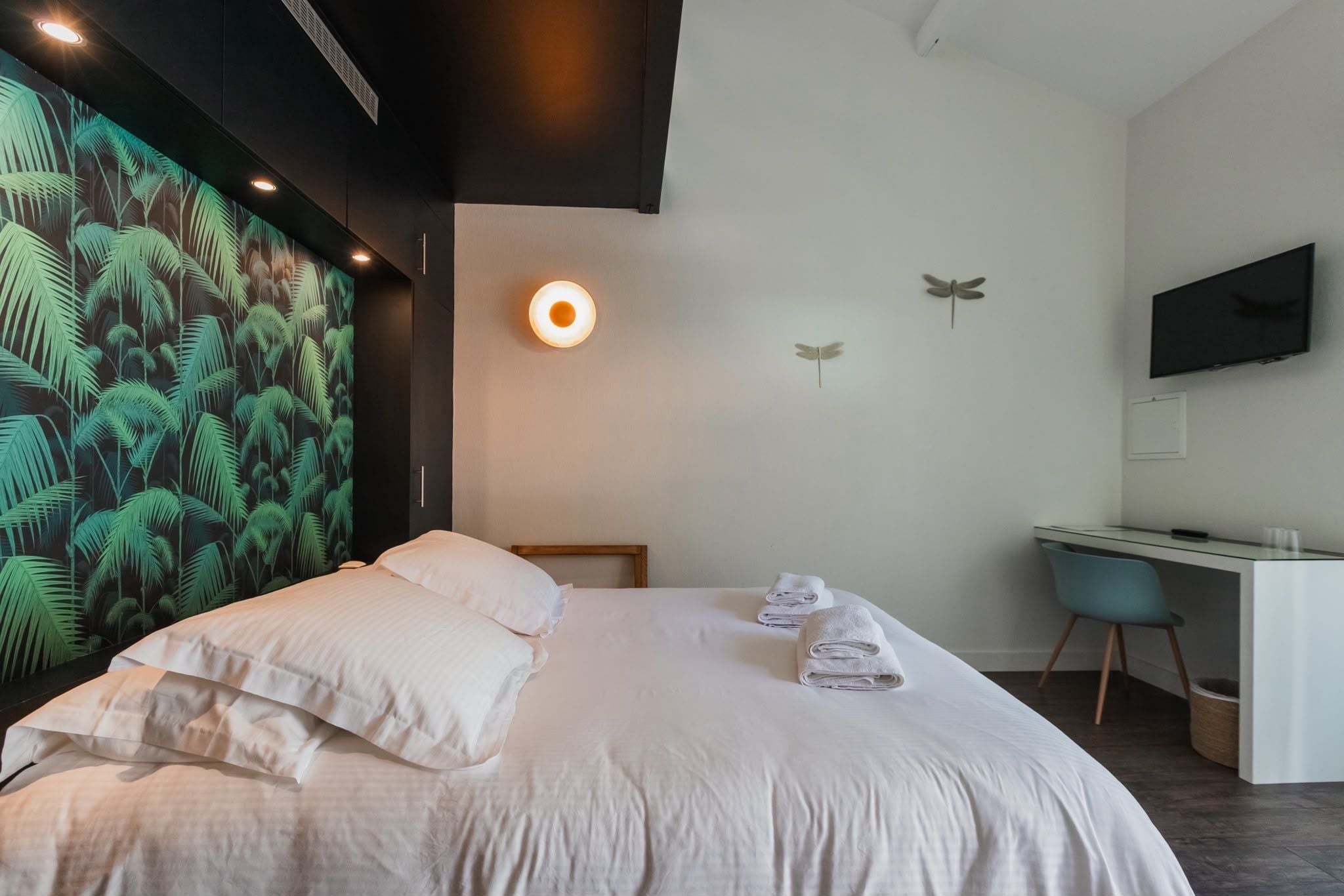 A modern hotel room with a bed, a desk, and a large wall mural.