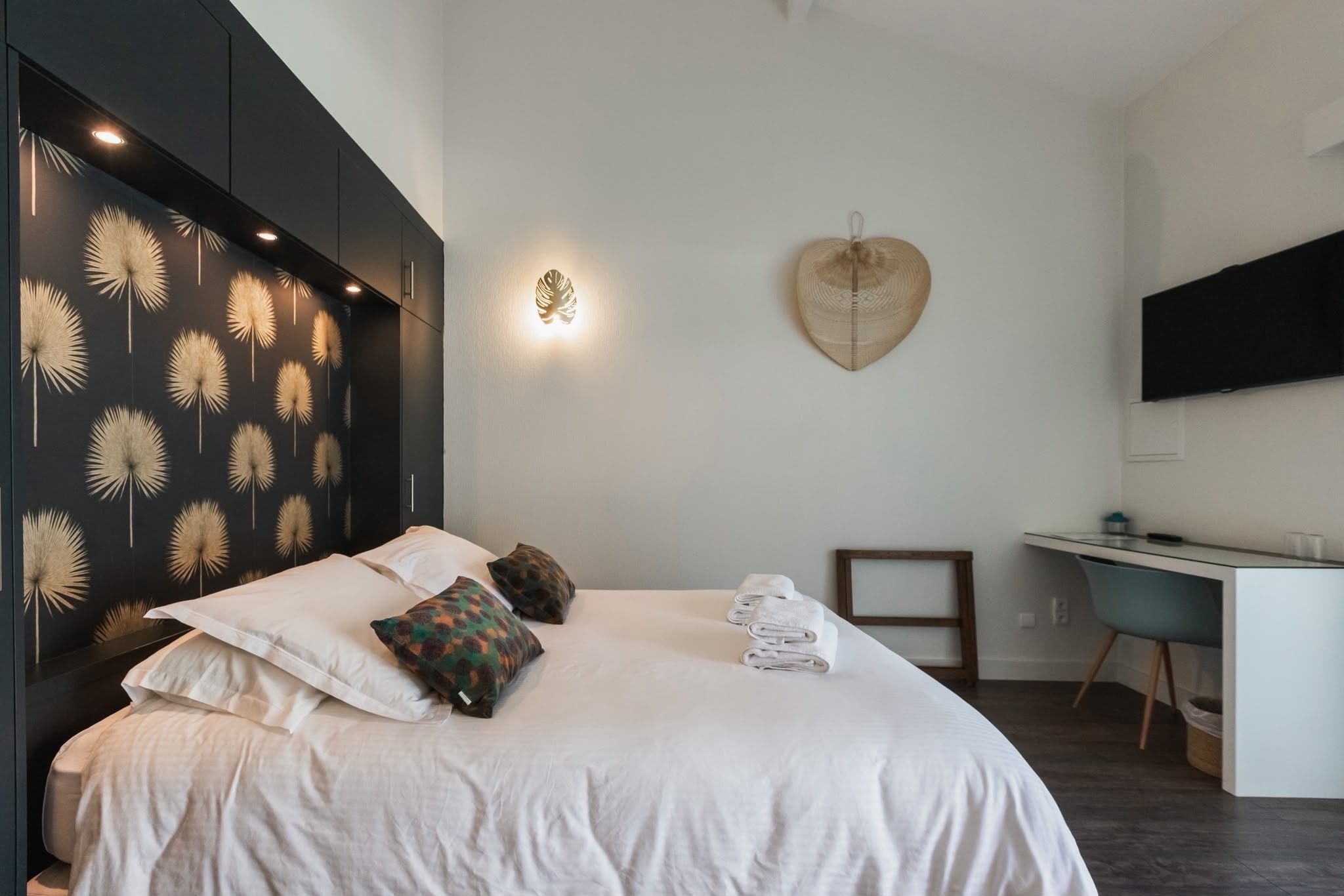 Un dormitorio moderno con cama, almohadas, un escritorio y un televisor montado.