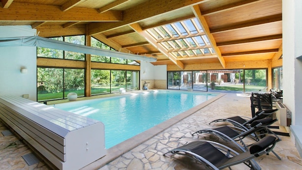 Una piscina interior con techo de madera, suelo de piedra y sillones de descanso.