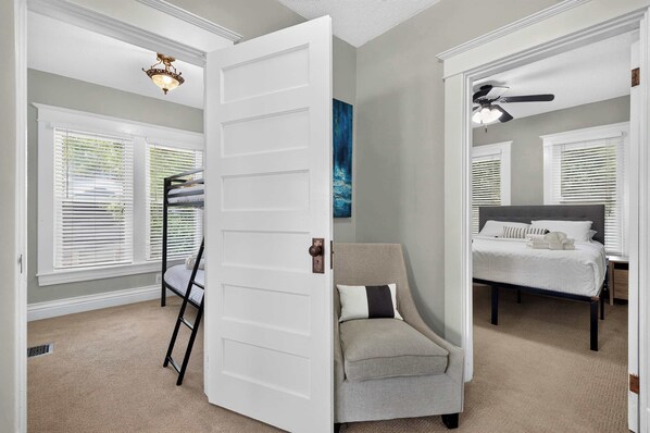 A bedroom with a bunk bed, a chair, a bed, and a ceiling fan.