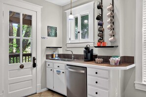 A kitchen with white cabinets, a dishwasher, a coffee maker, and a window with a view of trees.