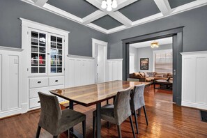 A dining area with a wooden table and chairs, white cabinetry, and a ceiling with exposed beams and pendant lighting.