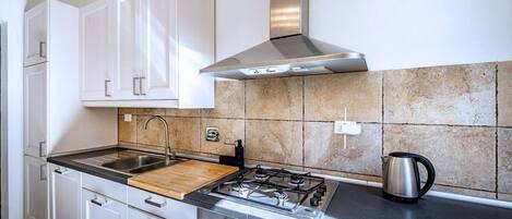 A modern kitchen with white cabinets, a gas stove, a stainless steel range hood, and a tiled backsplash.