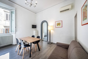 Un salon moderne avec une table à manger en bois, des chaises noires, un canapé marron, un lampadaire et un téléviseur fixé au mur.