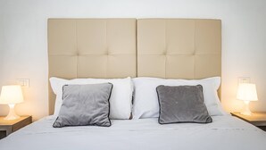 A bed with a beige upholstered headboard, two white pillows, and two gray pillows. There are two bedside lamps on either side of the bed. - Proconsolo A (Florence)