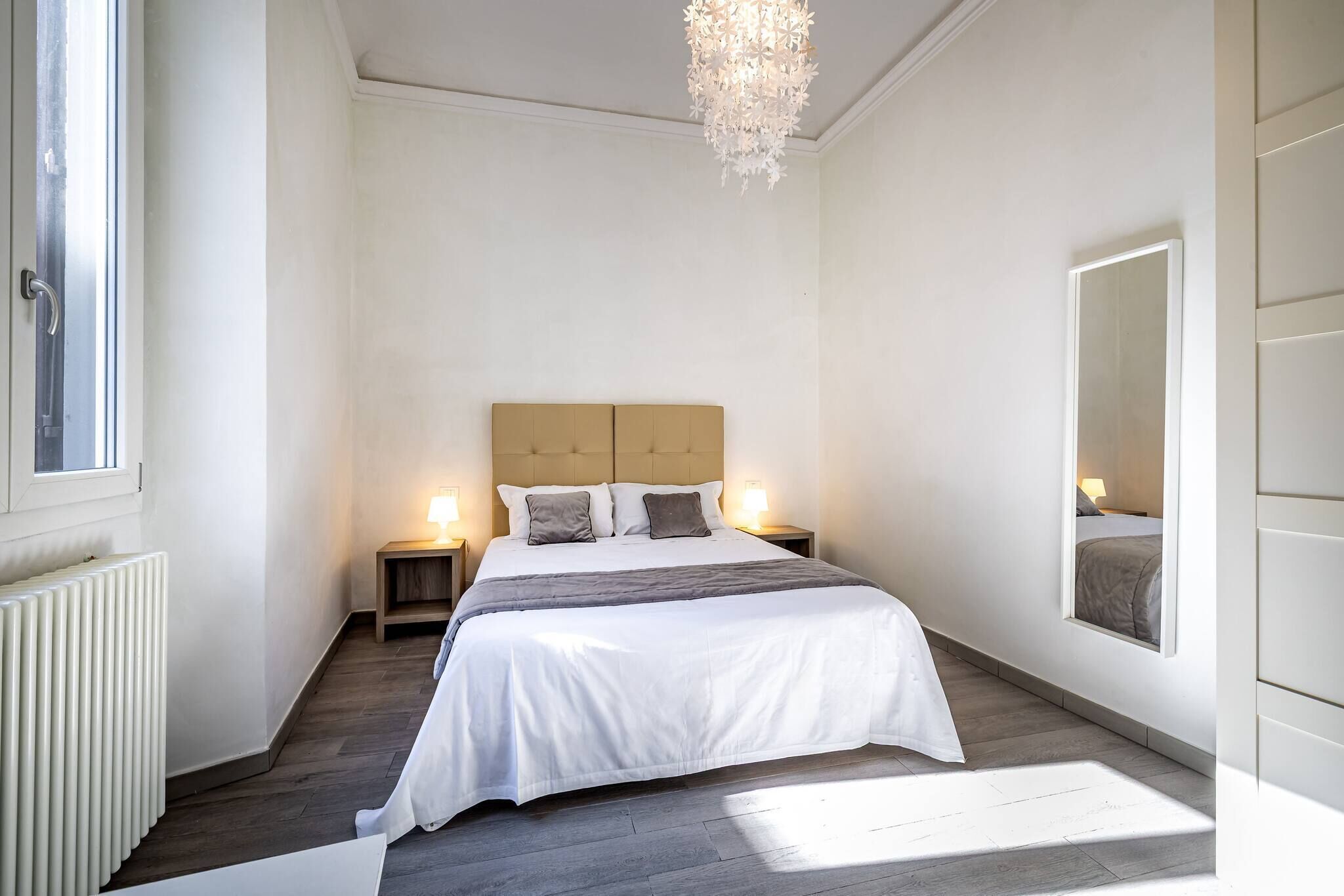 A bedroom with a large bed, bedside lamps, a radiator, and a window.