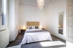 Een slaapkamer met een groot bed, bedlampjes, een radiator en een raam.