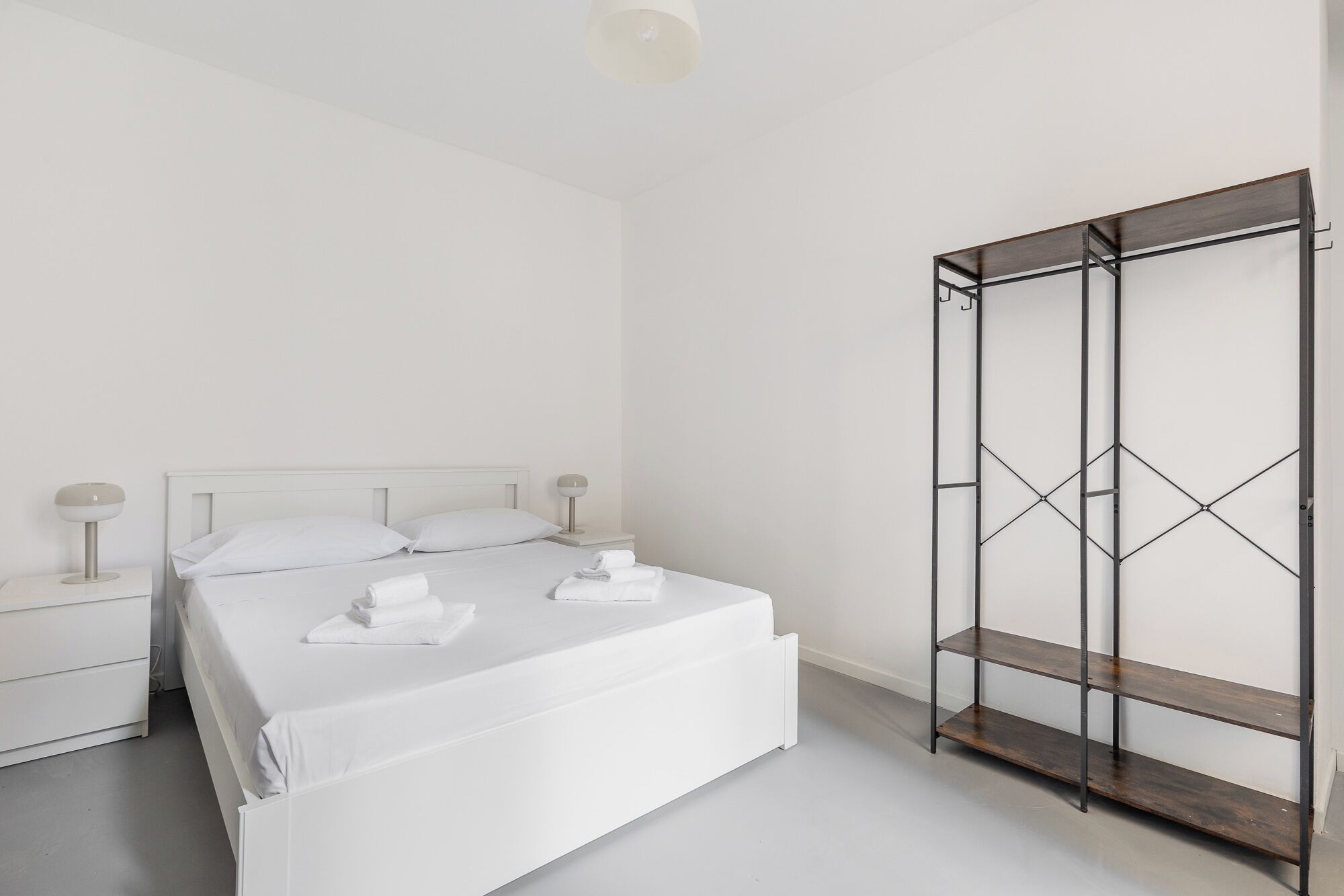 Un dormitorio minimalista con cama blanca, mesitas de noche y un armario metálico.