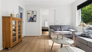 Moderni olohuone, jossa on puinen kaappi, harmaa sohva, pyöreä pöytä ja ikkuna, josta avautuu näkymä vehreään maisemaan.