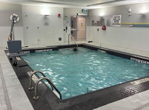 An indoor swimming pool with a shallow area marked, a lifeguard chair, and a pool ladder.