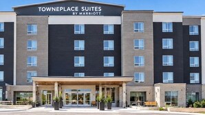 Un hotel de varios pisos con un diseño moderno, que presenta una entrada destacada con un corredor cubierto y un letrero que dice 'Towneplace Suites by Marriott'.