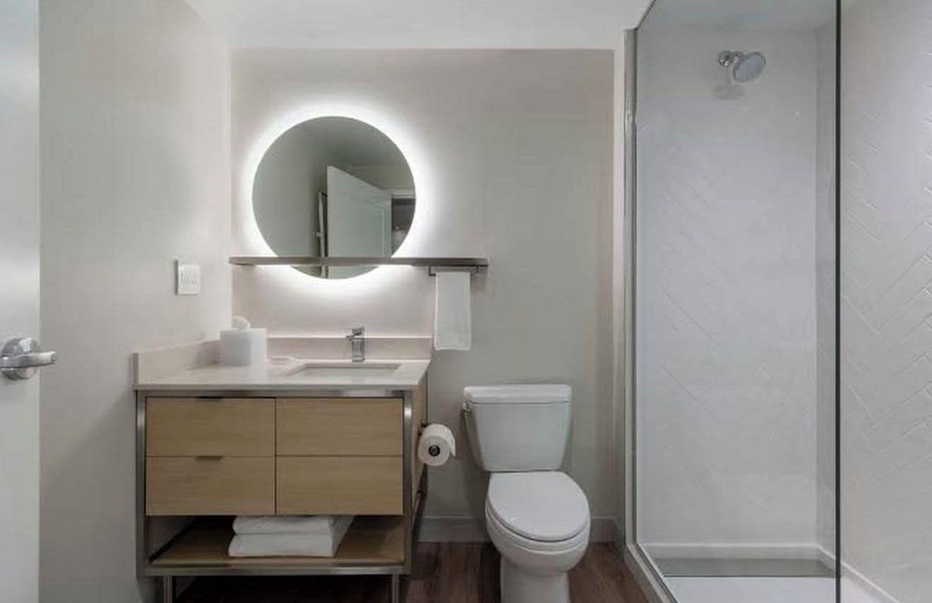 Un baño moderno con un espejo redondo, un inodoro y una zona de ducha.