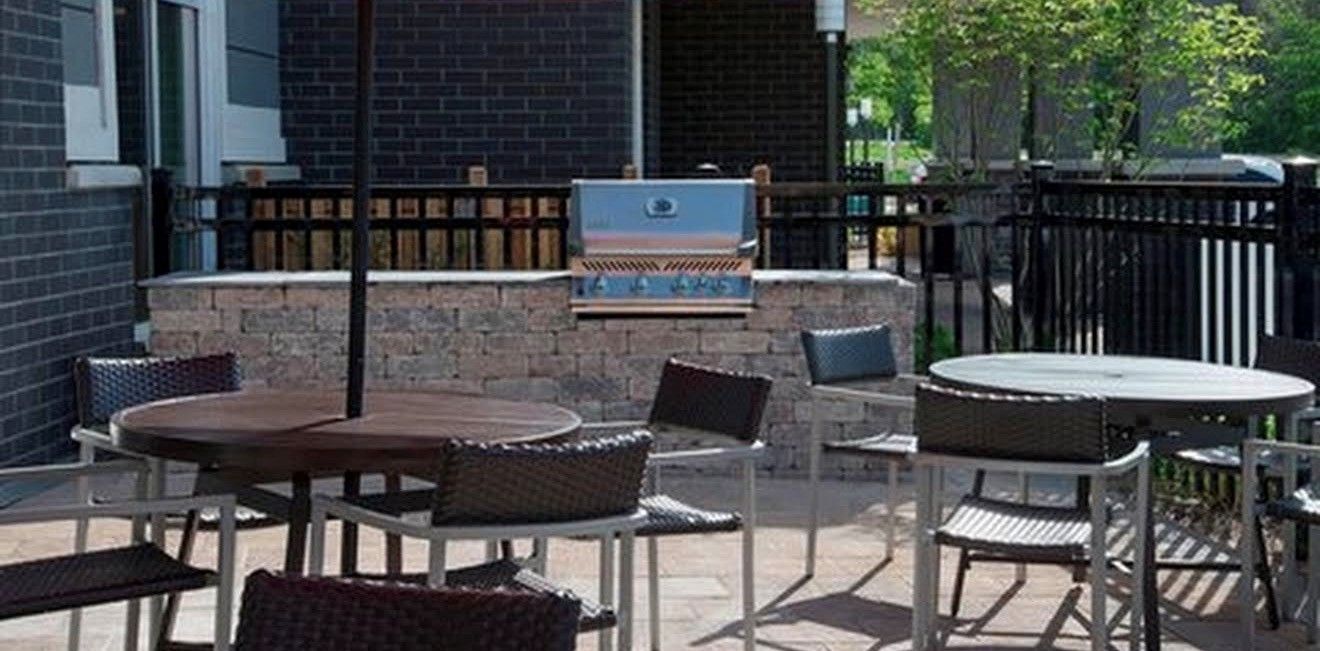 Un espacio al aire libre con patio, una parrilla, muebles de mimbre y un muro de piedra.