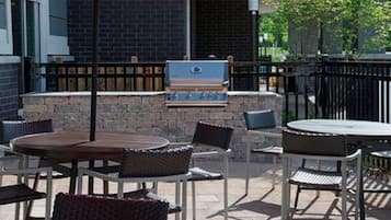 Un espacio al aire libre con patio, una parrilla, muebles de mimbre y un muro de piedra.