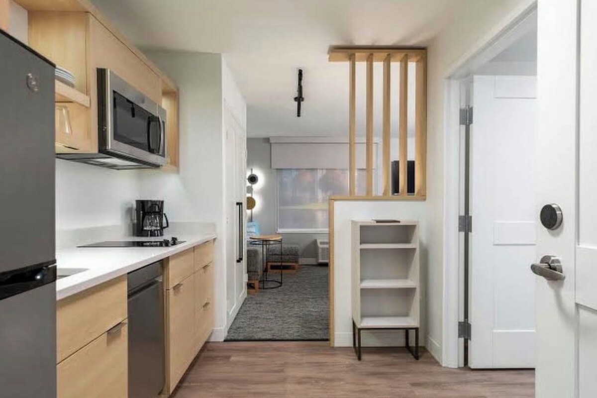 Una cocina compacta con electrodomésticos modernos, un comedor con una pequeña mesa y un estante empotrado.