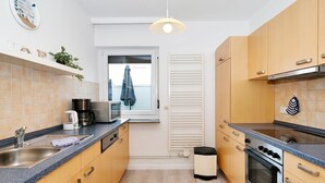 A modern kitchen with wooden cabinets, a built-in oven, a microwave, and a coffee maker. - Wellenklang – Your Cozy Vacation Rental Near the Sea (Büsum)