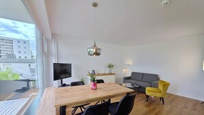 En moderne stue med spiseplads, en sofa, et fjernsyn og en balkon med udsigt til bygninger.